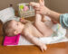 Mother changing diaper of adorable baby with a hygiene set for babies on the background